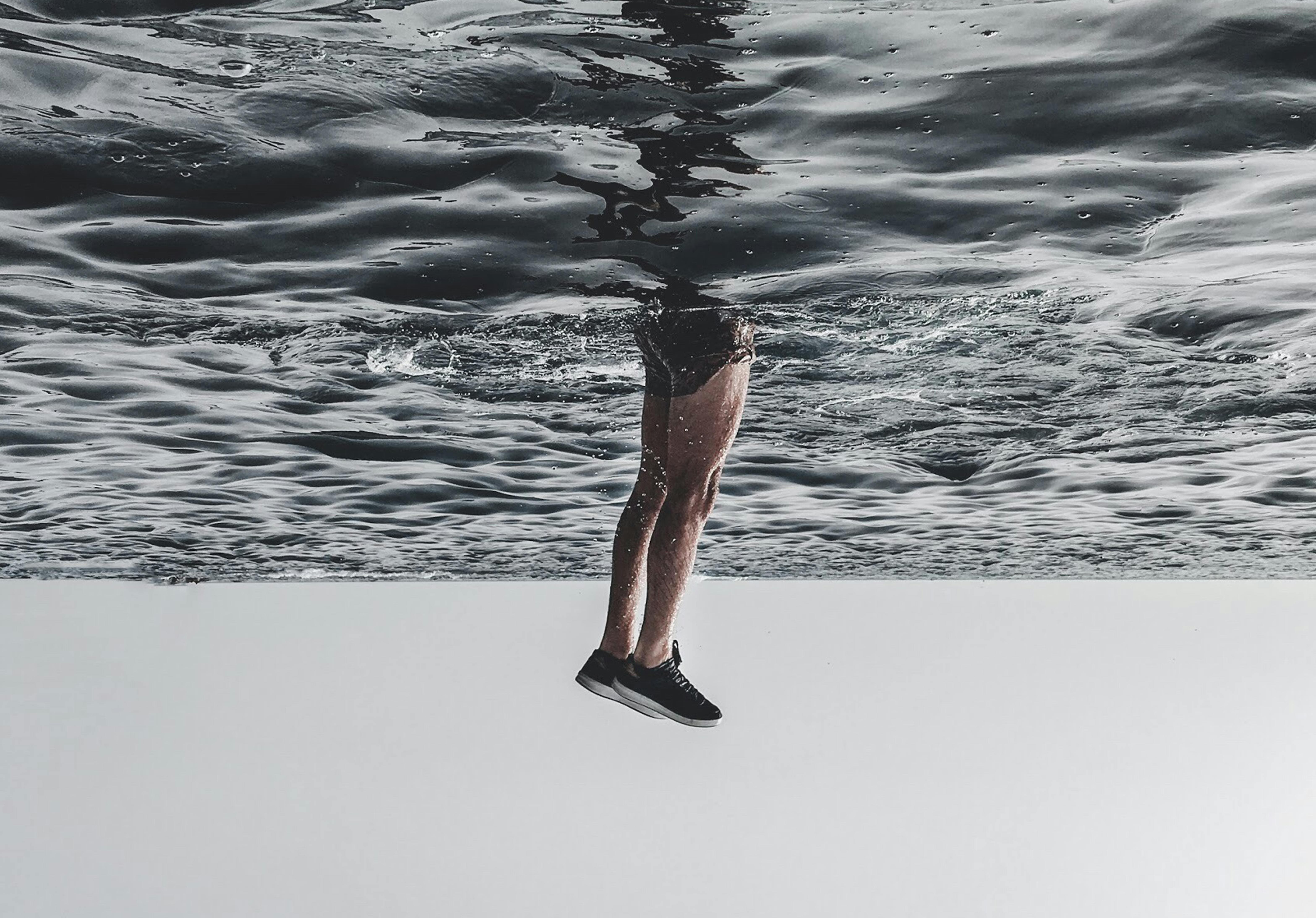 чоловік в морі, видно тільки його ноги в кросівках